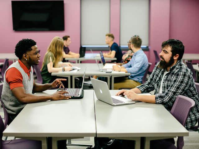 SBU students sitting at tables in classroom with laptops